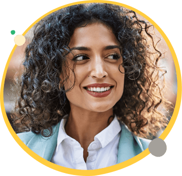 Woman smiling with dark brown curly hair looking to her right and wearing a white shirt with a teal overcoat.